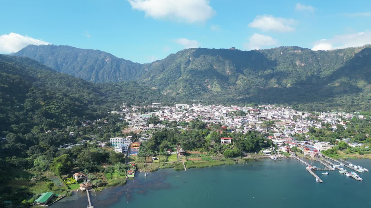 vista de avión no tripulado en guatemala volando sobre un lago azul rodeado de montañas verdes y volcanes y una ciudad en un día soleado en aitlan