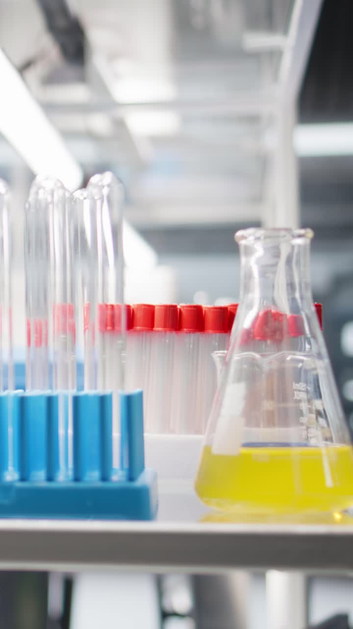Vertical video Close up of colorful chemical solutions inside scientific glassware on lab shelf