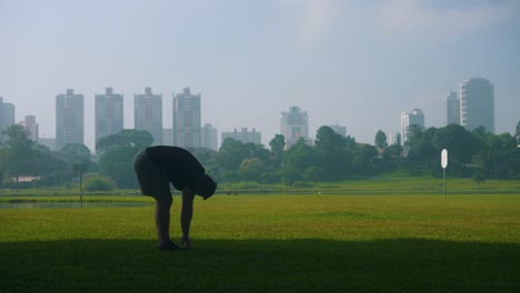 Stretching-training-young-man-exercising-on-grass-at-park-outdoors