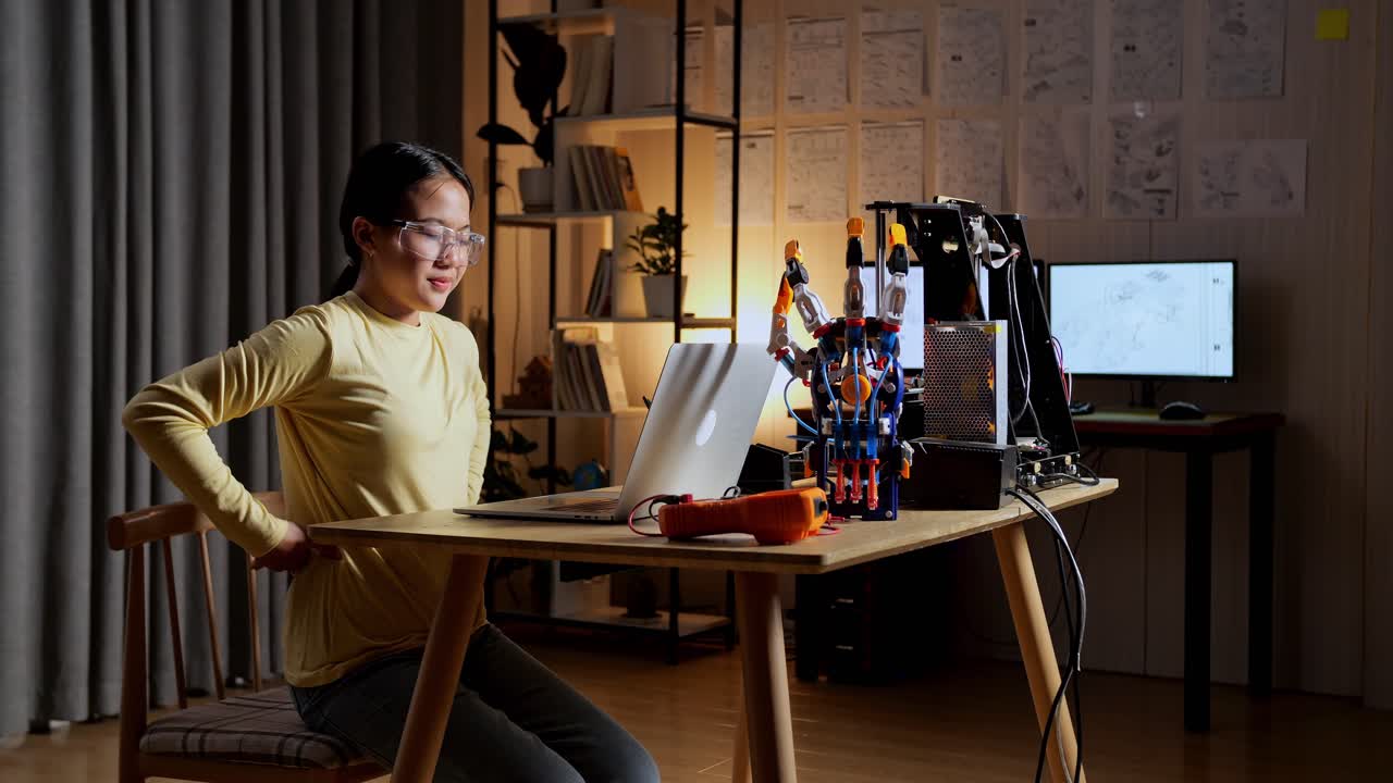 집에서 노트북을 사용하는 사이보그 손에 대해 작업하는 동안 허리 통증이 있는 십대 아시아 소녀