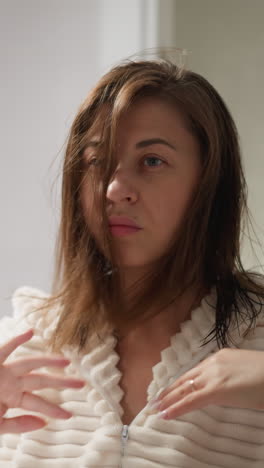 joven señora endereza el cabello oscuro con las manos en el baño claro. dama morena endereza el pelo oscuro después de la ducha en el baño luminoso acogedor cámara lenta