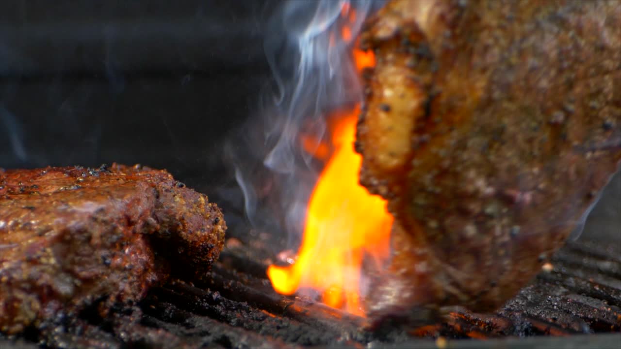 un par de pinzas para carne giran un jugoso filete de costilla casi cocido en una parrilla mientras llamas anaranjadas se disparan desde abajo