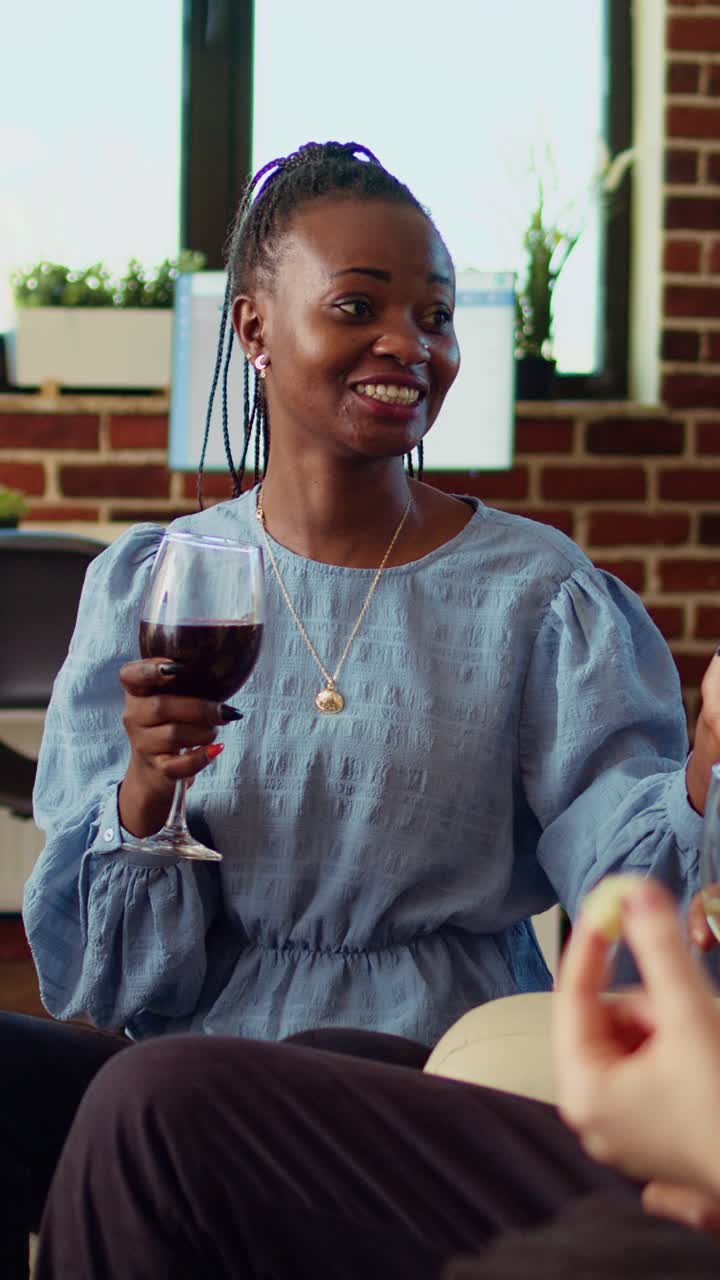 Vertical video BIPOC group of people chatting in living room, eating snacks and drinking alcohol