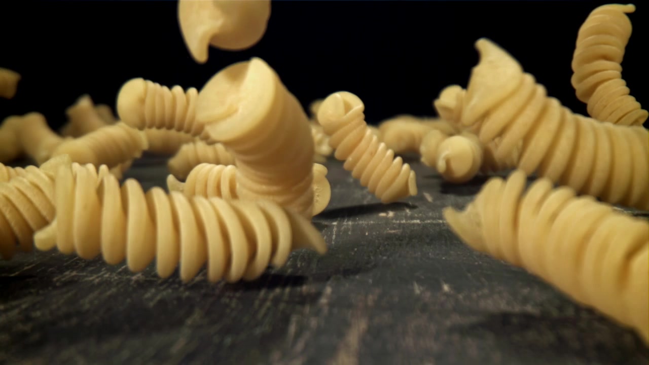 Fusilli secchi in caduta al rallentatore su una superficie scura.