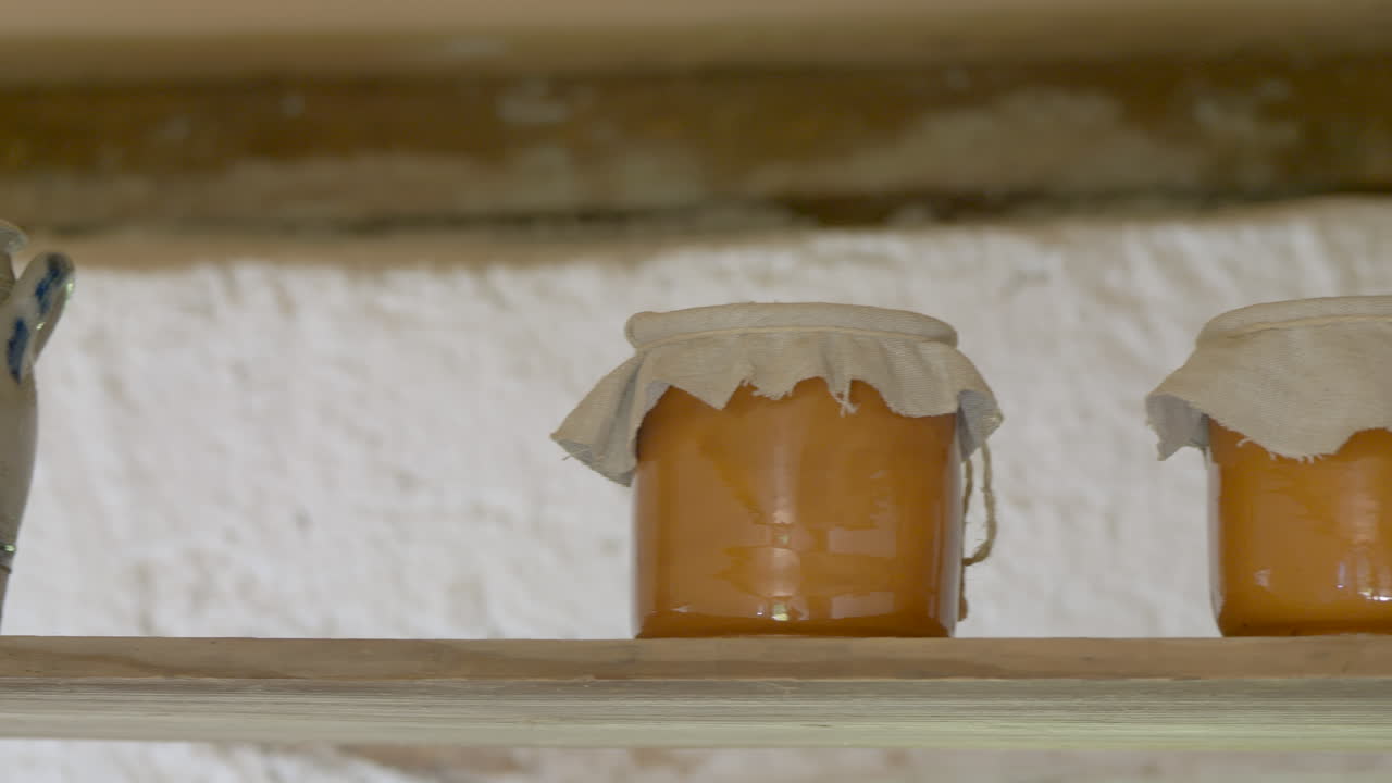 toma panorámica de una antigua cocina con una jarra antigua y miel hecha en vidrio colocada sobre una tabla de madera - época medieval