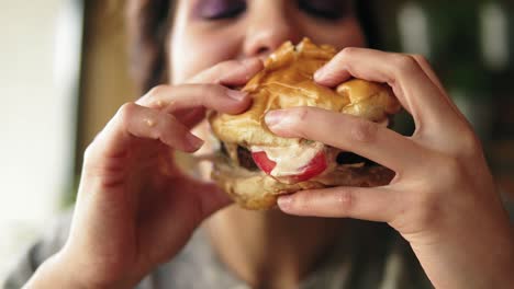 close up view of young woman biting big tasty juicy burger in cafe. slow motion shot