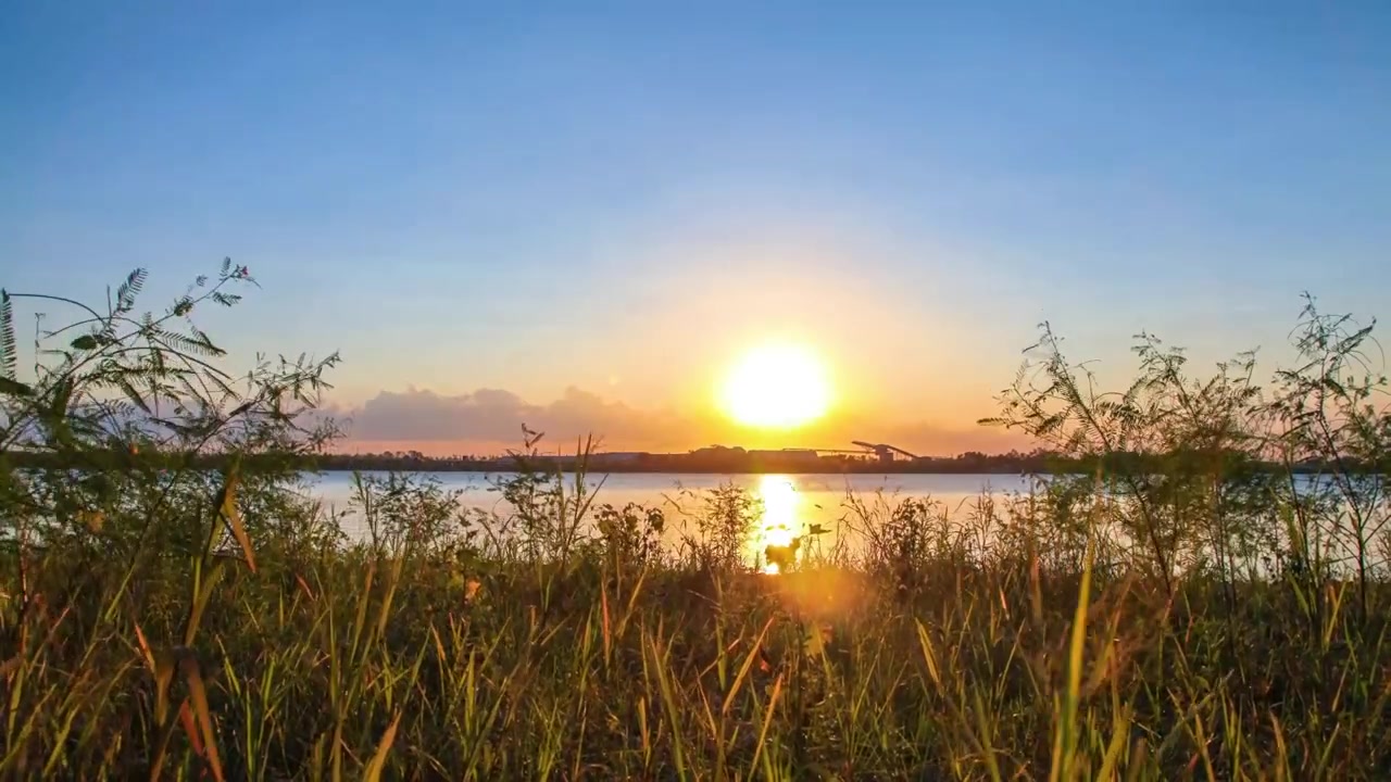 Timelapse af solnedgang med grønt græs i forgrunden og udsigt til en strømmende flod og skyer.