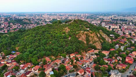 Toma-De-Drone-De-Una-Colina-En-Medio-De-Una-Ciudad-Con-Una-Estatua.