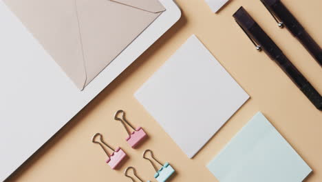 overhead view of notebook, pens and stationery arranged on beige background, in slow motion