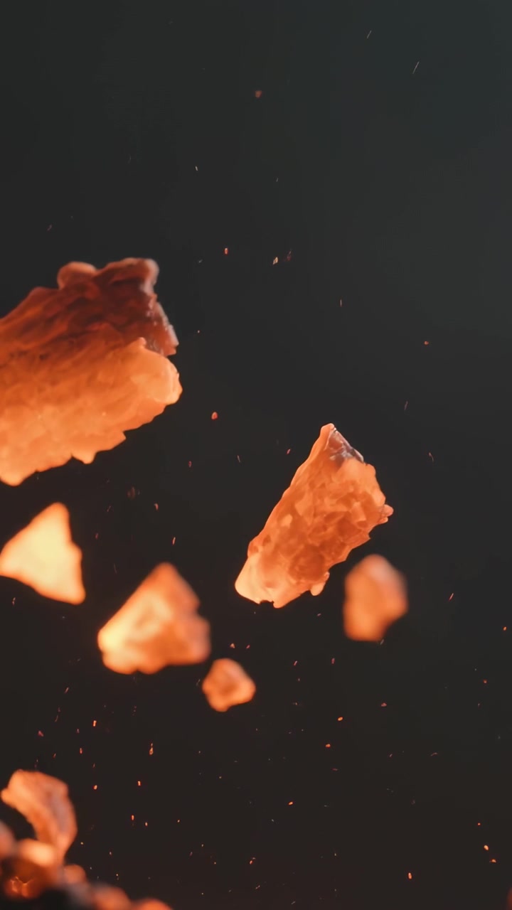 Vertical video: Moving tan crumbs drifting, rotating, sending sparks as frames shifting on dark set