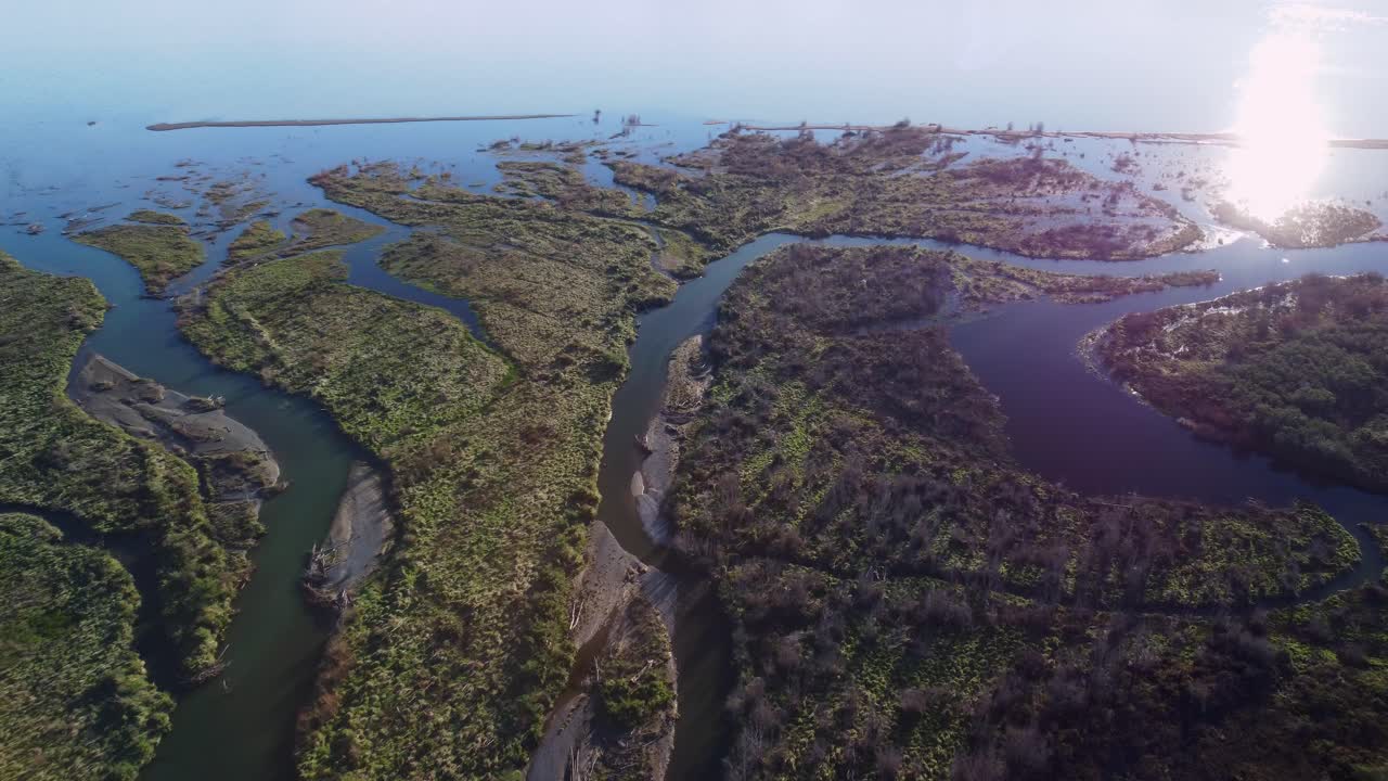 volando sobre una desembocadura de un río y un humedal junto a un lago al atardecer