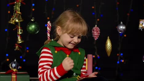 Kid-girl-in-Christmas-elf-costume-doing-shopping-online-using-mobile-phone,-browsing-on-social-media