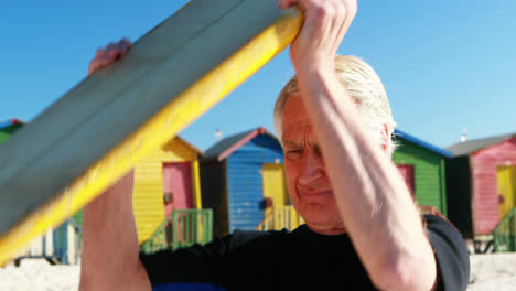 hombre mayor en traje de buceo llevando una tabla de surf sobre la cabeza