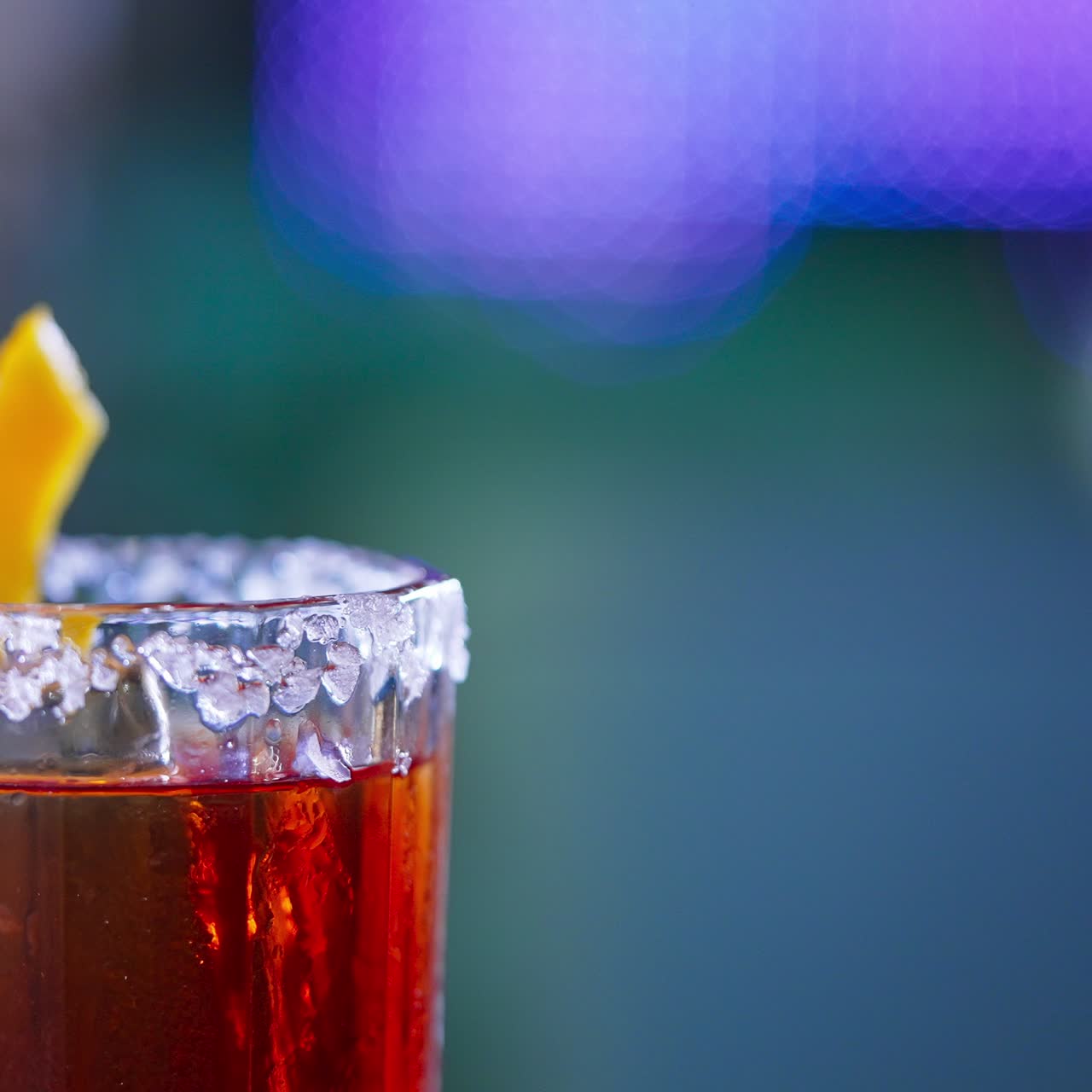 Rotating glass with top decorated with salt and orange peel. Red alcohol cocktail in the bar. Close up. Blurred backdrop