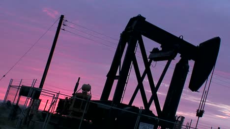 an oil derrick pumps against a purple sky