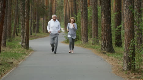 Happy-Elderly-Man-And-Woman-Smiling-And-Running-Along-Pavement-In-Park