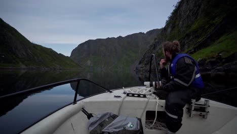 norwegian seated on the front edge of his boat while sailing in peaceful lake of norway