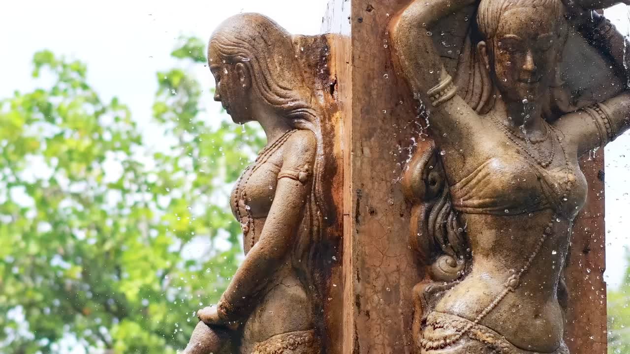 Close-up of a bronze statue with water droplets, set against a lush green background.