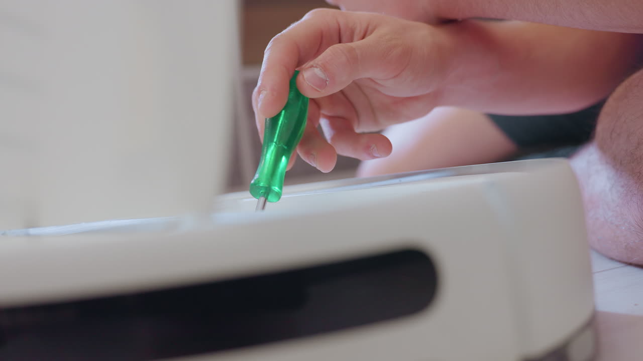 Close up of technician hand holding green screwdriver repairing vacuum robot showing careful precision and focus on maintenance process with professional approach to solving technical