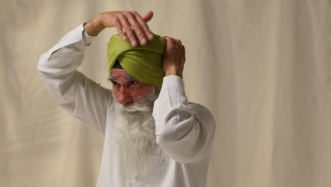 fotografía de estudio de un anciano sikh con barba atando tela para un turbante contra un fondo plano 2
