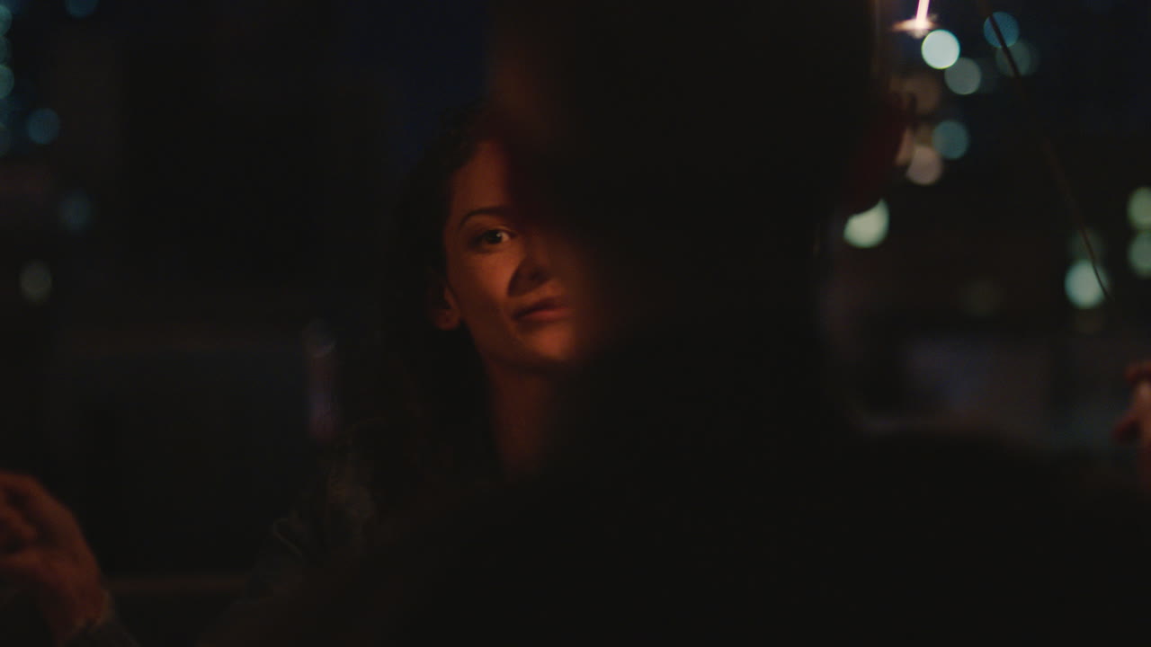 feliz pareja caucásica besándose en la azotea por la noche sosteniendo bengalas celebrando el aniversario disfrutando de una romántica velada urbana