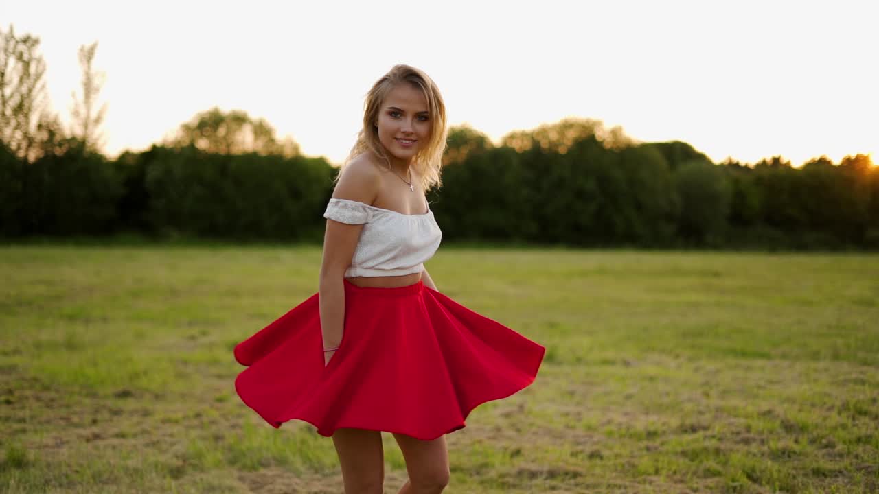 Bella ragazza bionda che volteggia in un vestito rosso durante un tramonto all'ora d'oro.
