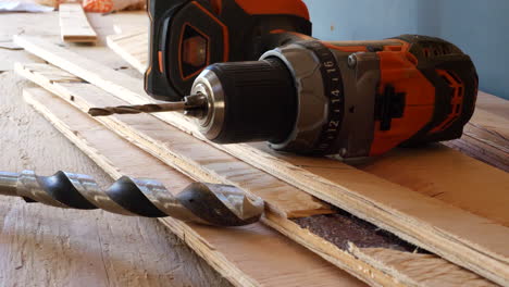 un taladro de herramienta eléctrica en una pila de tableros de madera contrachapada con una broca en un sitio de construcción