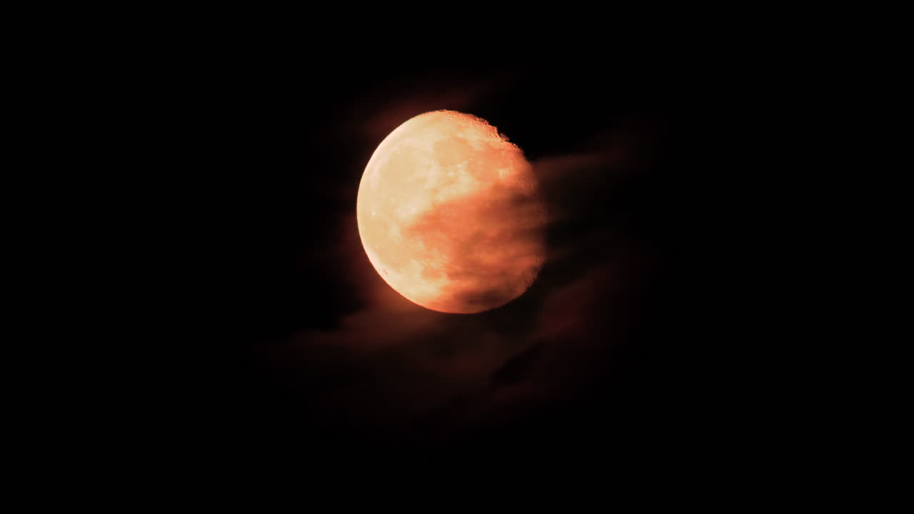 A golden full moon partially covered by drifting clouds in the night sky