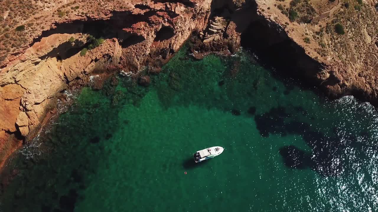 vista aérea hacia abajo en cámara lenta de un solo barco blanco navegando en un océano tranquilo y silencioso con agua brillante debido a la luz del sol rodeada de montaña en benidorm en españa