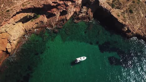 Aerial-downward-slow-motion-view-of-a-single-white-boats-sailing-in-calm-and-silent-ocean-with-shining-water-due-to-sunlight-surrounded-by-mountain-in-Benidorm-in-Spain