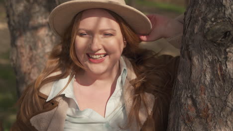 portrait of a pretty smily red haired woman wearing a camel hat in the forest