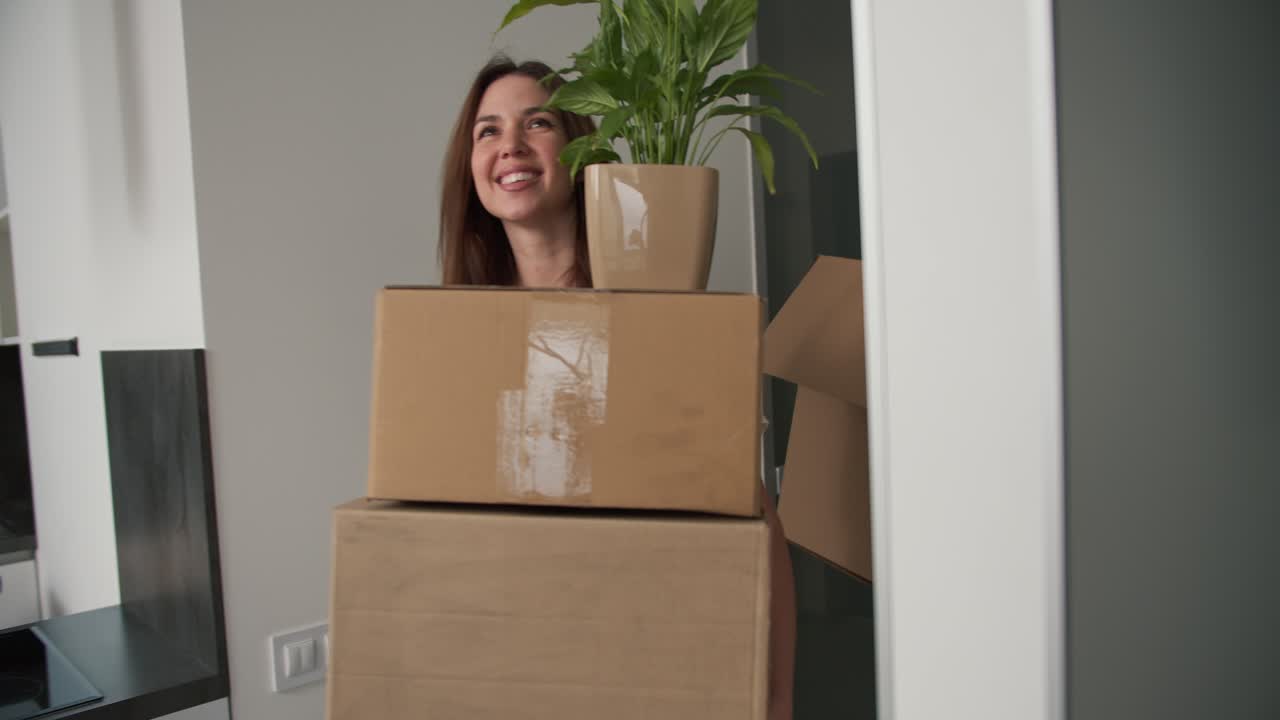 una feliz chica morena junto con su novio entra en un nuevo apartamento sosteniendo grandes cajas de madera y plantas de la casa en sus manos en su nuevo apartamento comprado