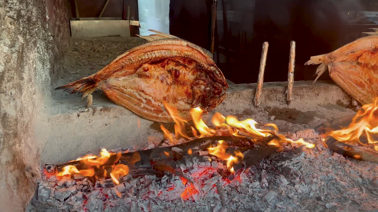 Bream fish at an Iraqi restaurant butterflied, smoked, skewered, and grilling over a fire pit and coals