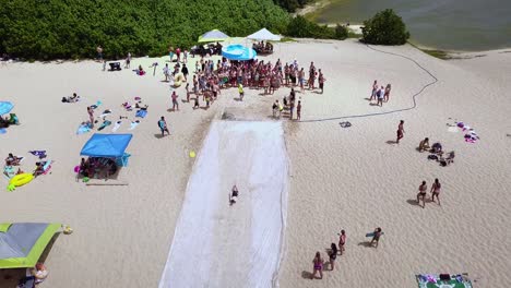 drone shot following a couple people sliding down a waterslide on the beach down to the water at waimea bay, hawaii.