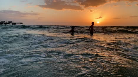 two kids swimming - jumping waves in the ocean on the beach during sunset in florida