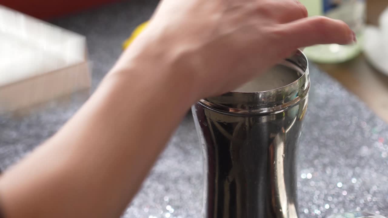 Donna che lascia cadere ghiaccio in uno shaker Cobbler per cocktail a casa usando una vaschetta per cubetti di ghiaccio per preparare un cocktail o una bevanda mista