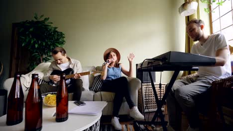 emotional young people from musical band are holding rehearsal in home studio getting ready for performance. they are singing and playing keyboard and guitar.