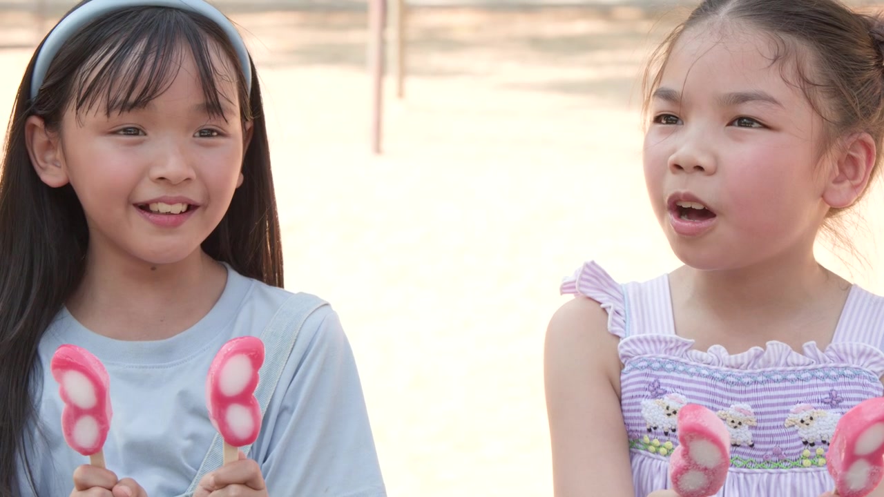 日当たりの良い公園で、2人の幼い少女がピンクの蝶の形をしたアイスキャンディーを楽しんでいます。