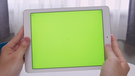 hombre con las manos sosteniendo una pantalla verde (clave de croma) tableta inteligente en su habitación