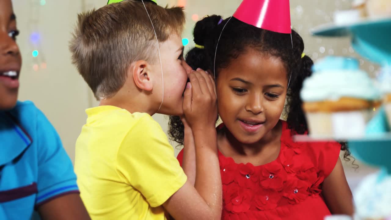 Boy whispering to girl while sitting with friends during birthday party 4k