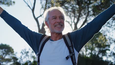 senior man standing with arms up in the forest 4k
