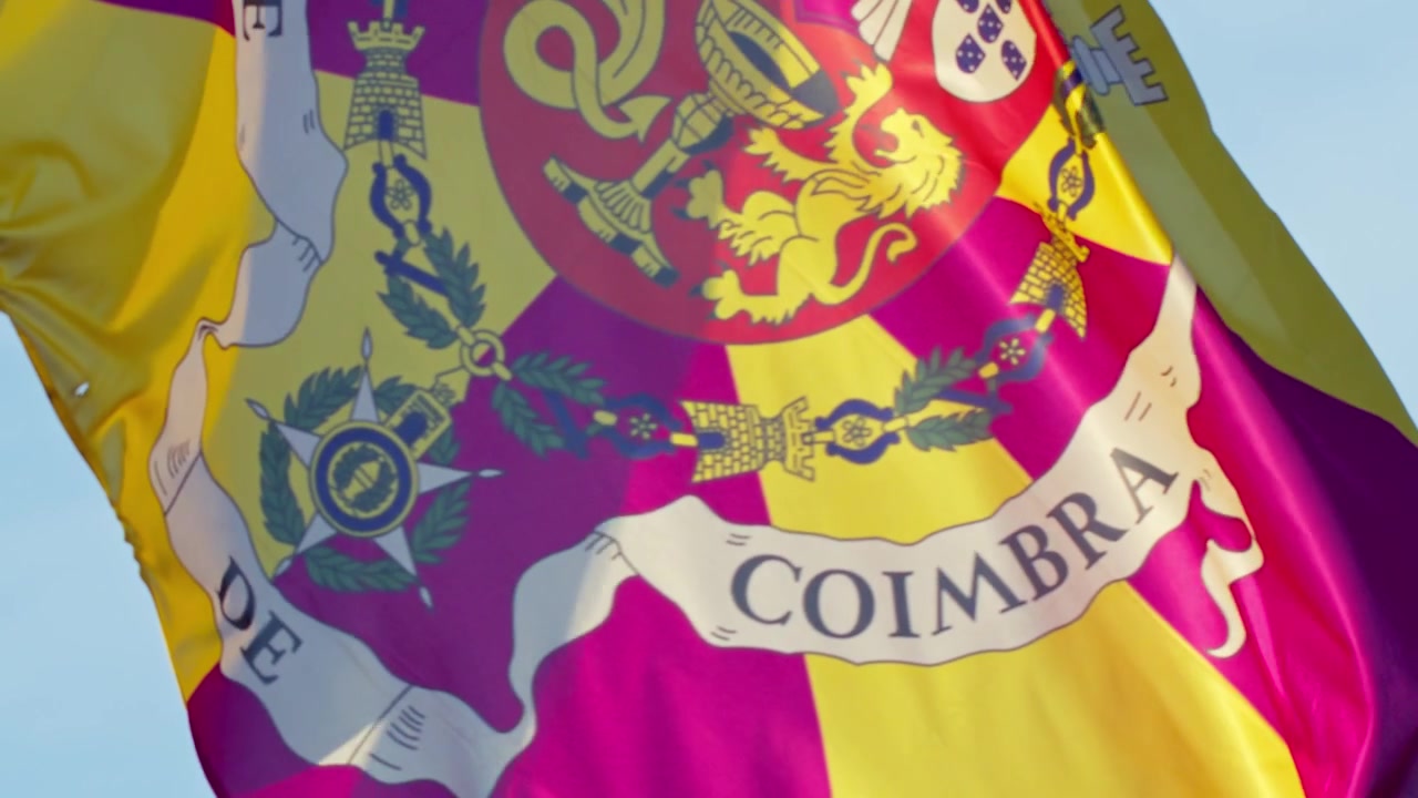 Grande plano da bandeira colorida de Coimbra a ondular suavemente com a brisa sob um céu azul brilhante em Portugal.