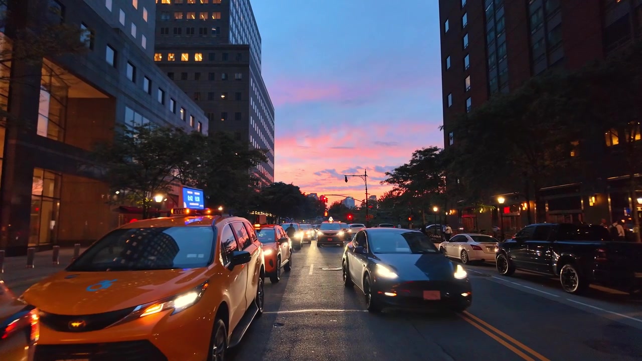 Nova York, EUA, 5 de junho de 2026: Táxis em uma rua de Manhattan ao pôr do sol, Nova York. A composição ao nível da rua inclui carros estacionados, letreiros iluminados, semáforos vermelhos e nuvens rosadas.