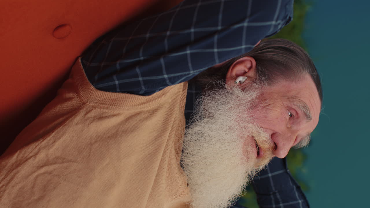 무선 이어폰을 착용한 행복하고 편안한 남자가 춤을 추고 좋아하는 음악을 듣고 집 소파에서 잠을 자고 있습니다.