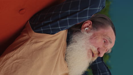 hombre feliz y relajado con auriculares inalámbricos bailando escuchando música favorita, durmiendo en el sofá de casa