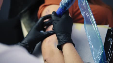 woman tattoo artist holding tattoo gun, filling it with blue ink, working on hand tattoo. gloved hand holding tattoo gun working on modern body art. artist working on female's hand. slow motion