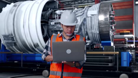 asian male engineer with safety helmet working on a laptop while standing with airplane engine maintenance conducted, analytics checking the turbine