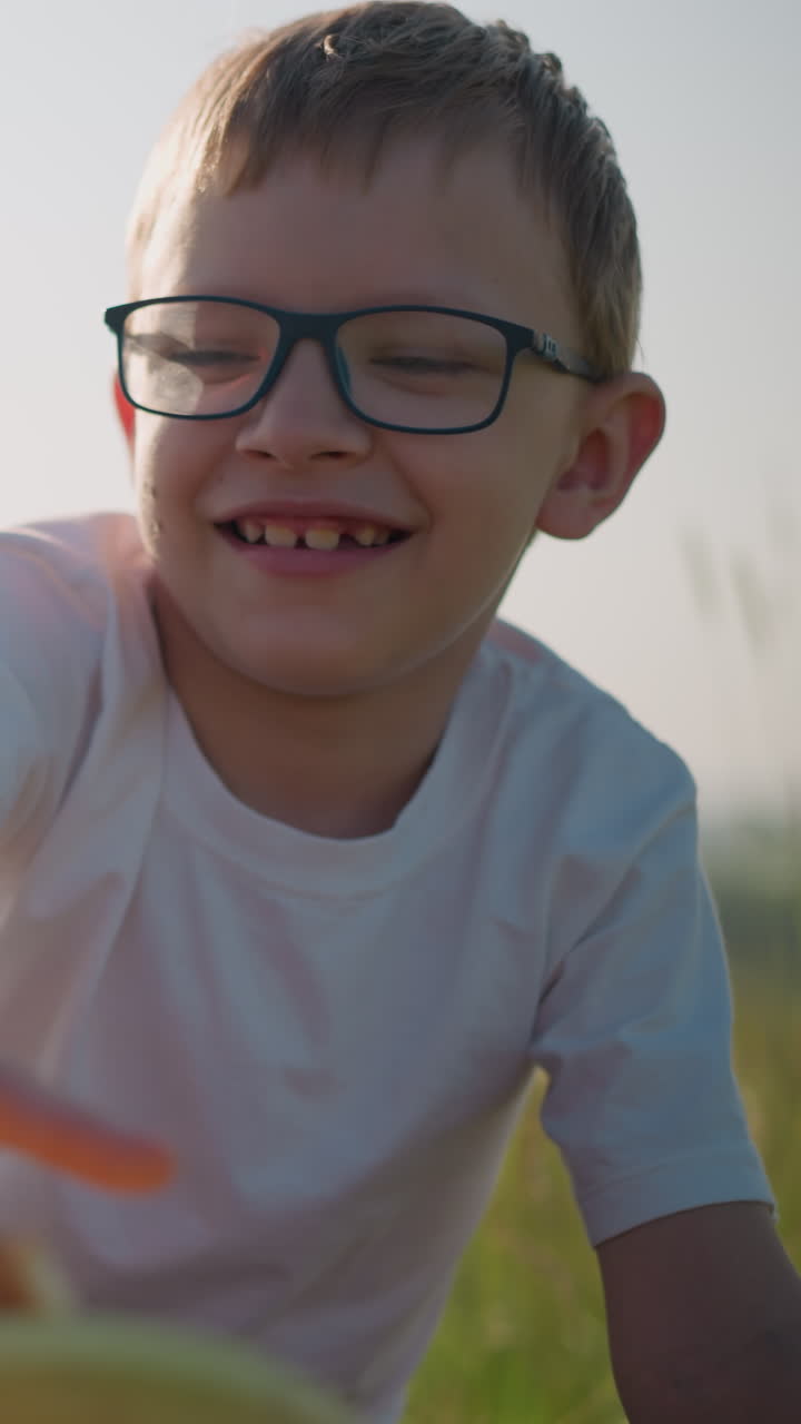 un niño alegre con gafas y una camisa blanca se extiende para agarrar algo de una canasta mientras su madre, sosteniendo una manzana roja, toca juguetón su mano para detenerlo