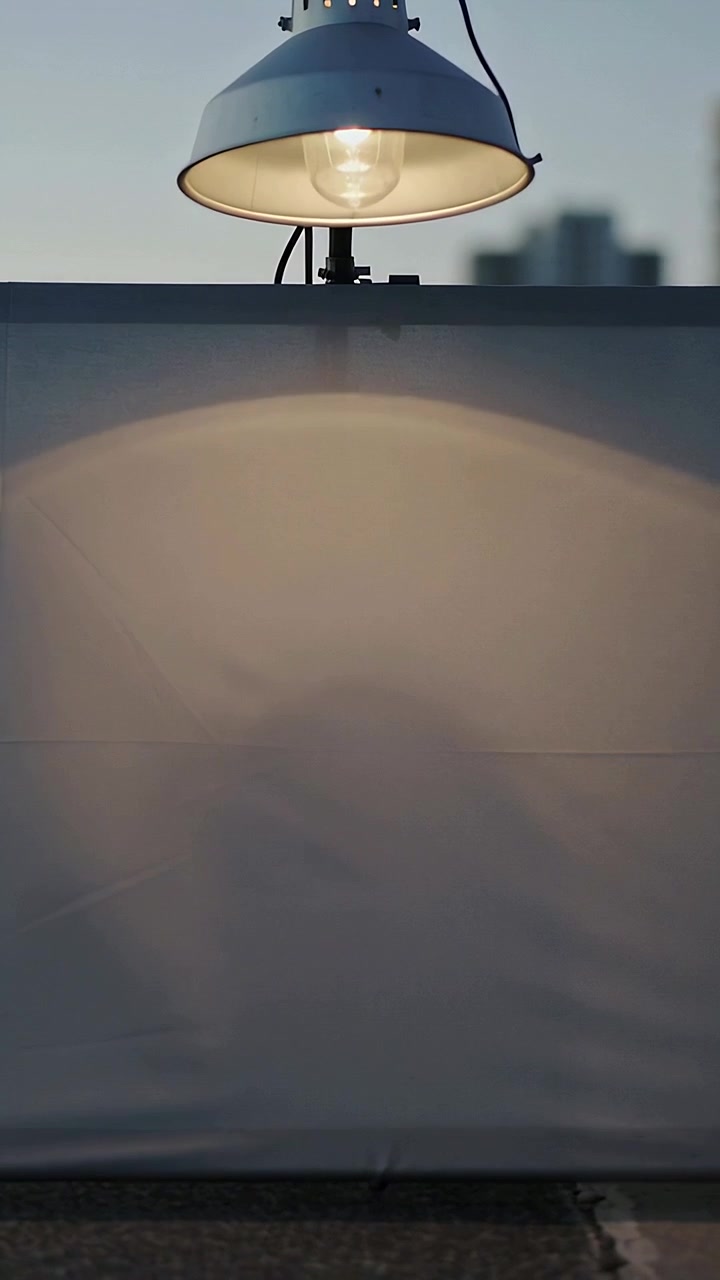 Vertical video: Turning on dome work lamp casting oval on sheet on roof revealing moving shadow