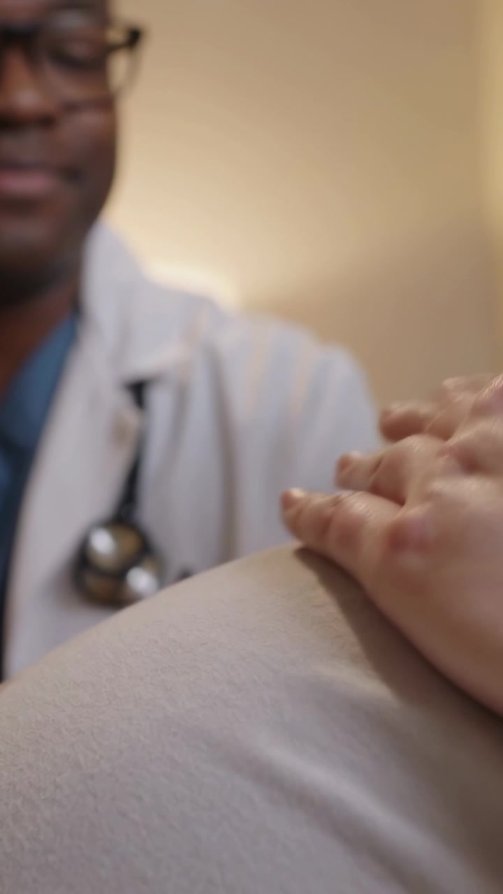 Vertical video: Leaning clinician palpating pregnant belly in clinic with stethoscope for checkup
